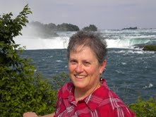 Photo of Diane Swords, in plaid shirt, outdoors in front of waterfalls