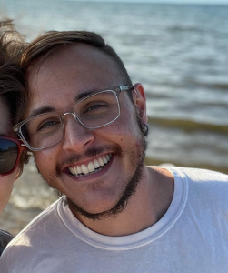 Photo of Jersey Cosantino, smiling, wearing eyeglasses with lake in the background